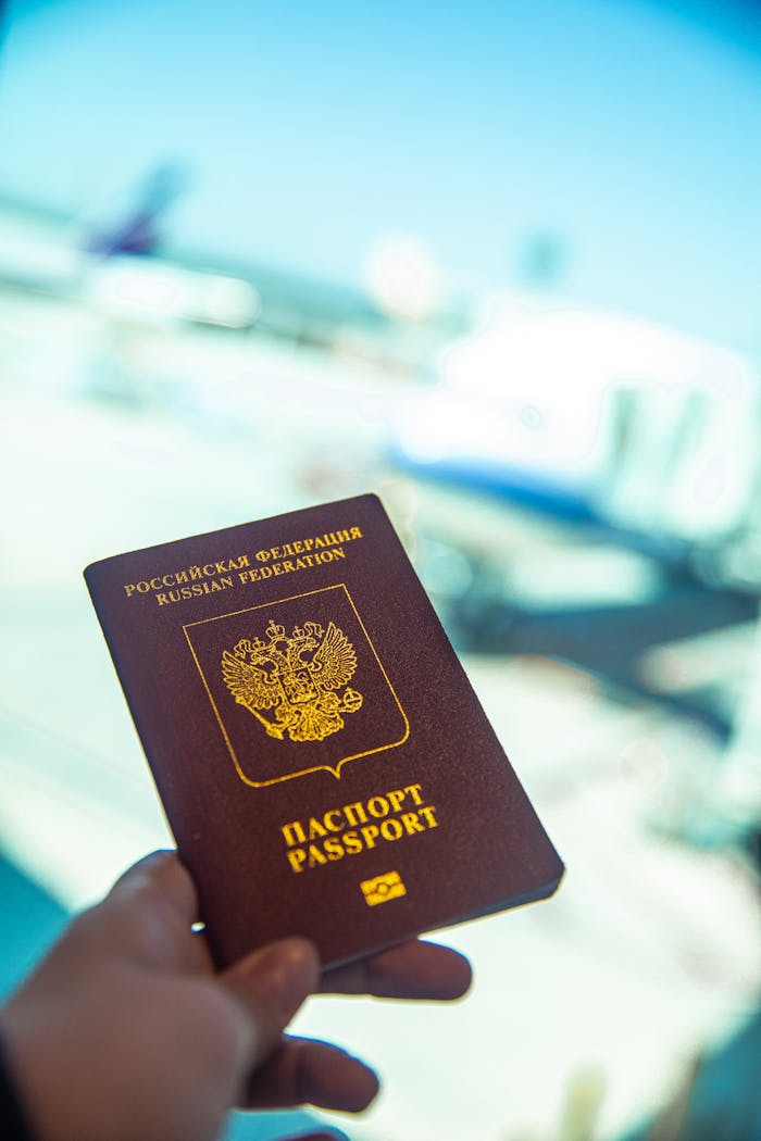 client-satisfaction-img Close-up of a Russian passport being held near an airport gate window with blurred aircraft in the background.