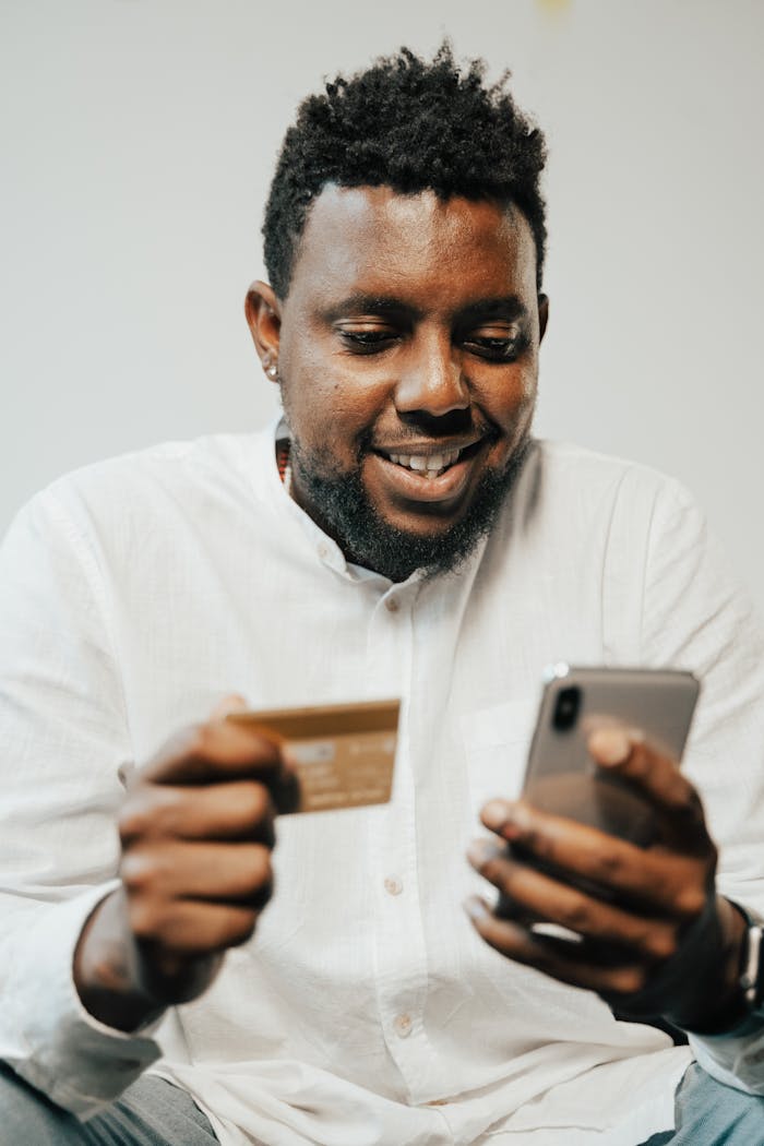 Smiling man using smartphone and credit card for online shopping indoors.